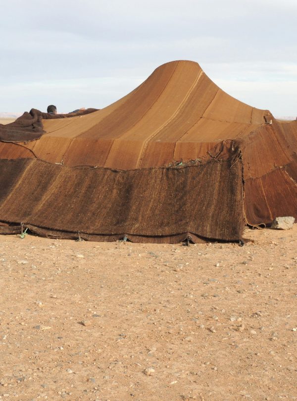 Brown nomadic tent set in a barren desert landscape under a clear sky.